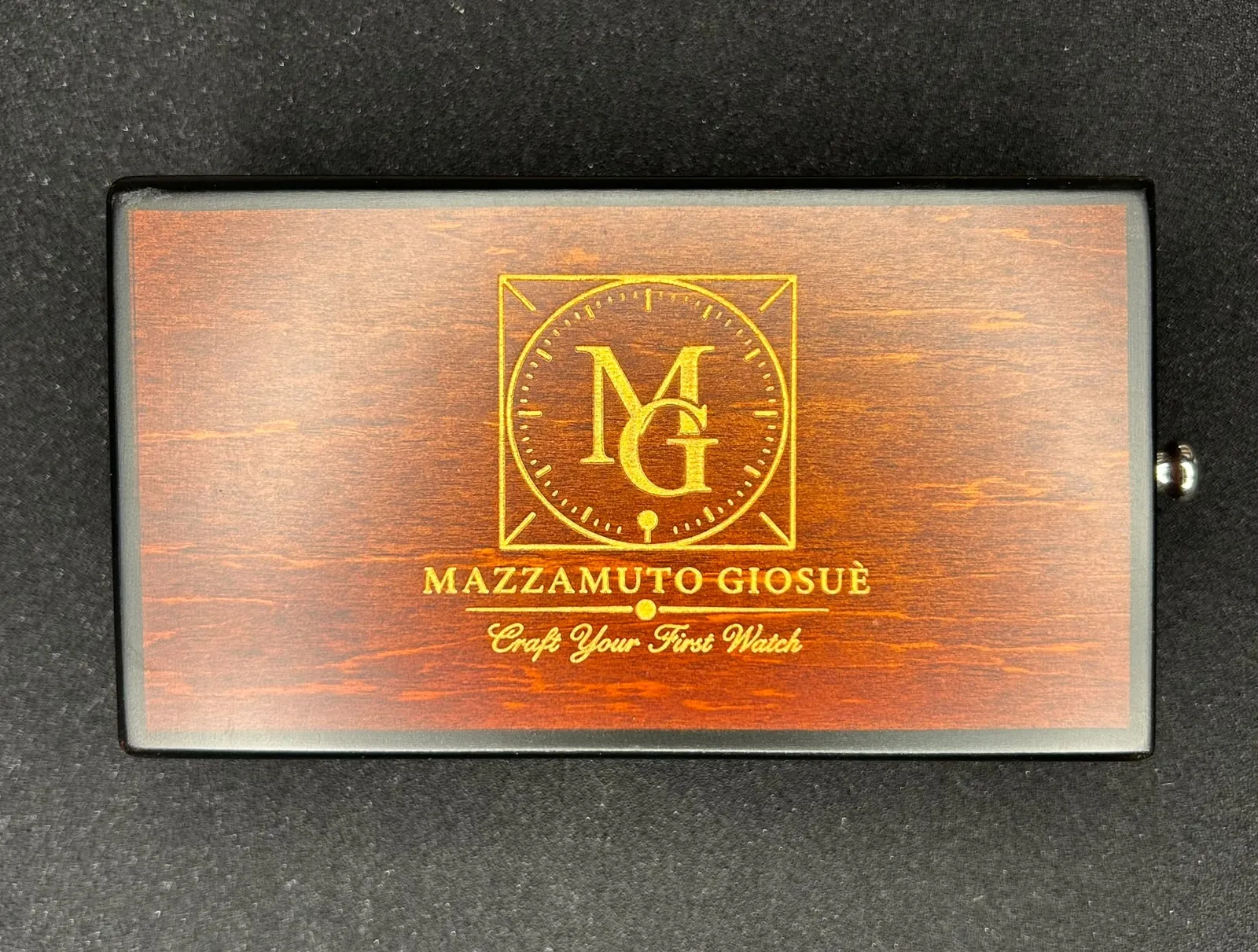 Le coffret fermé, vu du dessus : monogramme MG doré sur le couvercle, avec les inscriptions « Mazzamuto Giosuè » et « Craft Your First Watch ».